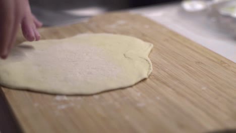 caucasian hands pick up flat tortilla dough, flip over and press on wood board