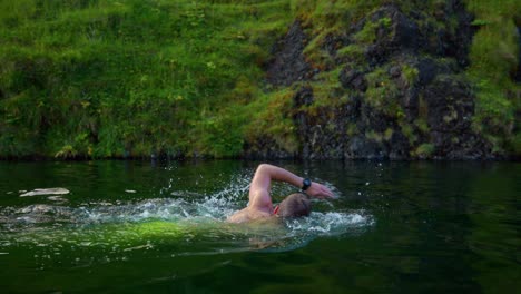 Tourist-Swimming-In-The-Seljavallalaug-Pool-With-Moss-Covered-Rocks-At-The-Backdrop-In-Southern-Region-Of-Iceland