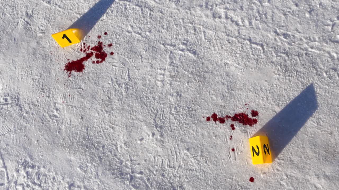Top view of numbered evidence markers beside red blood stains on winter snow covered road or pathway