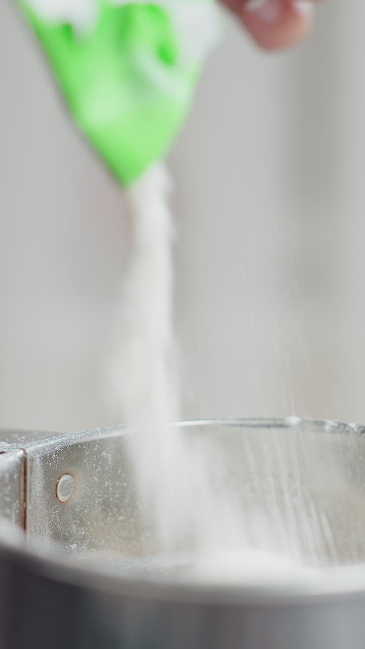 은 밀가루가 금속 컵에 여 부드러운 가루 구름을 만들어내는 클로즈업 모션은 밝은 빛에서 기 준비의 정밀성을 강조합니다.