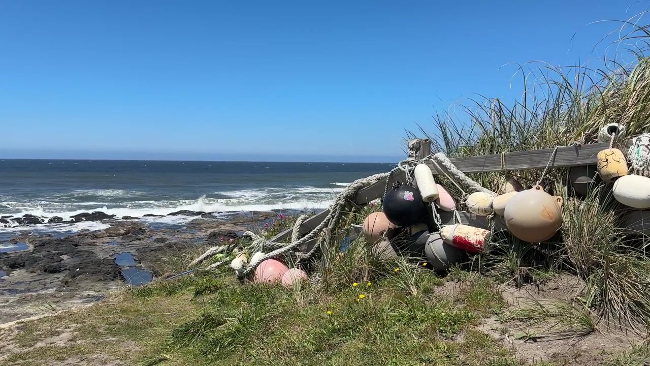 Reb-bundne bøjer og flåd hænger fra et vejrbidt hegn over en stenet Oregon-kystlinje, med tidevandsbassiner og brændende bølger langs Stillehavskysten