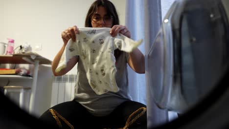 pregnant woman opens washing machine and places baby clothes into it. fpv, inside