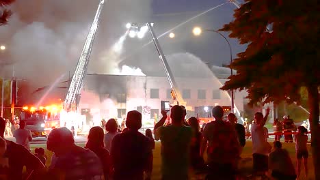 people watch firefighters control building fire with water from fire trucks at night on street in montreal, quebec.