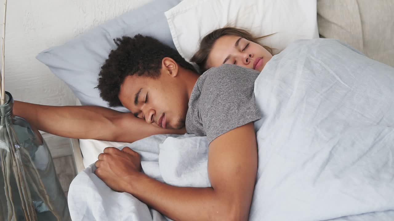 Close Up view of multiracial couple lying in bed and sleeping while embracing each other. Young family concept