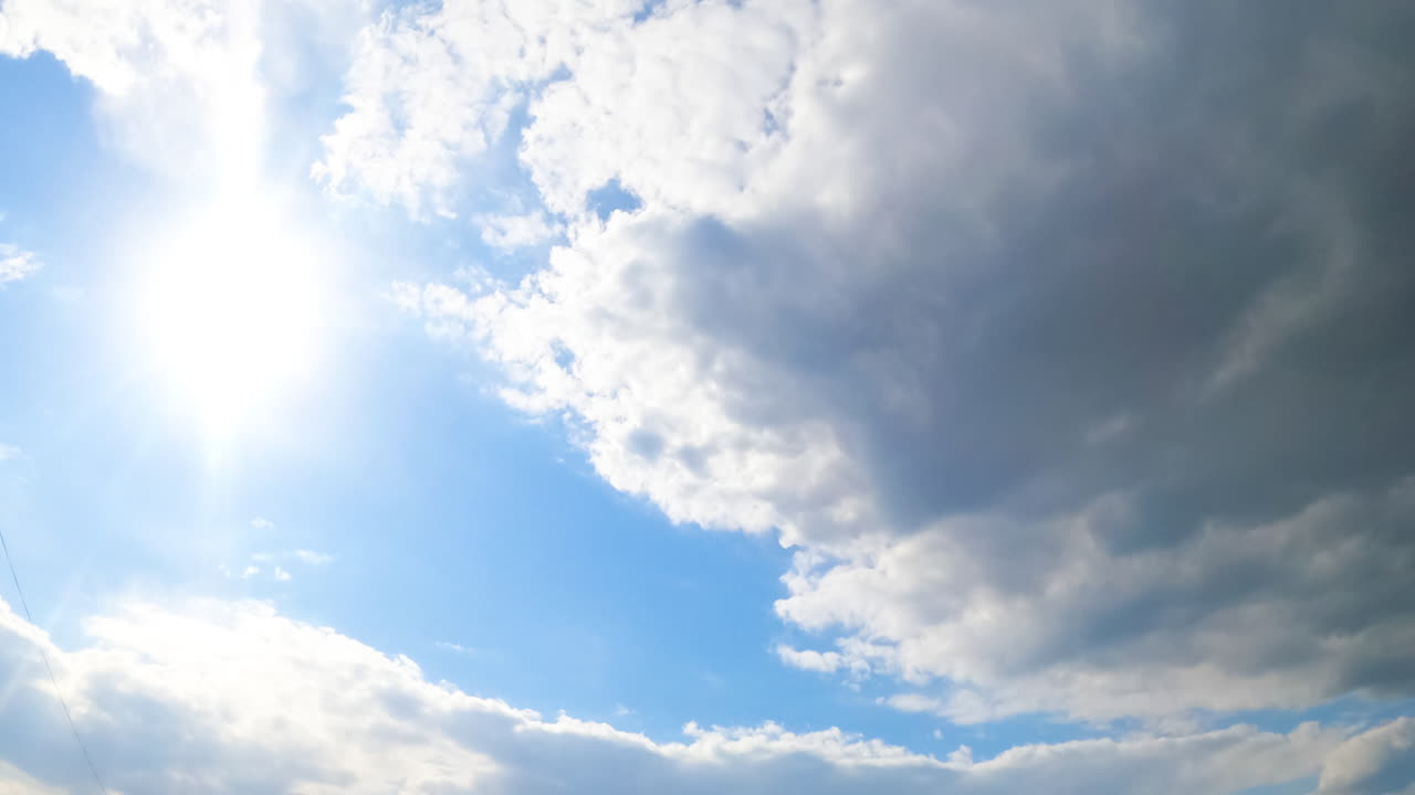 Bright sun in the blue summer skies. Big grey cloud approaches to hide the sun. View from below. Timelapse.