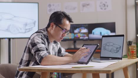 vista lateral de un hombre asiático dibujando un nuevo concepto de diseño de automóvil en una tableta en el estudio con televisión y computadoras muestra modelo de automóvil eléctrico 3d