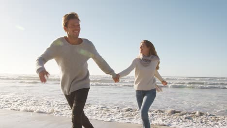 pareja divirtiéndose corriendo a lo largo de la playa de invierno juntos