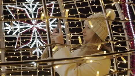 woman photographing colorful christmas decorations with a phone at night