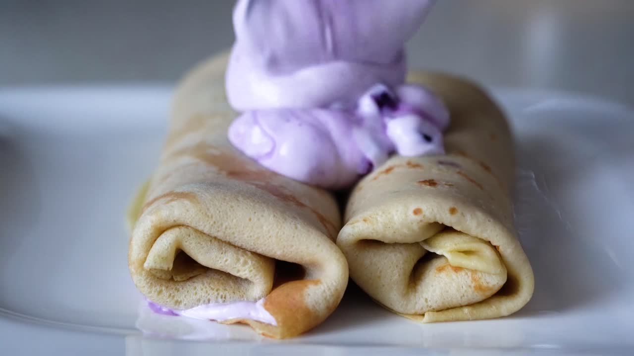 dos tortitas francesas enrolladas decoradas con crema de arándanos morada de colores en un plato blanco
