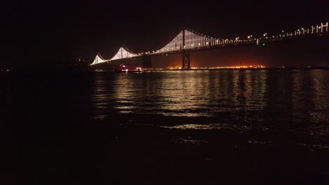 gimbal tilting up shot of a ferry under the bay bridge at night in san francisco, california