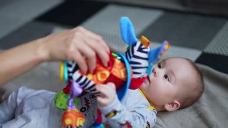 playful little boy attracted by a colorful soft toy. mother showing a bright toy to her infant baby. close up.