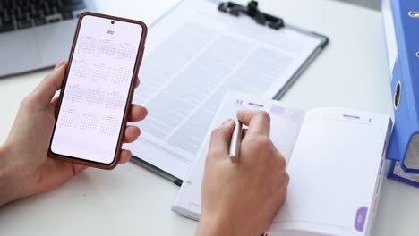 woman holds smartphone with calendar for 2022 and makes business plan for next year 4k movie