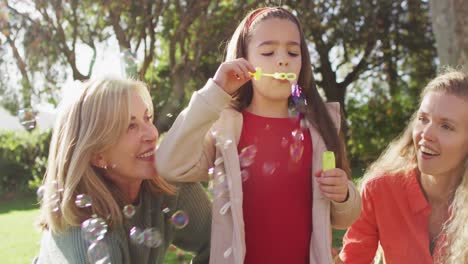 video of happy caucasian daughter blowing bubbles with mother and grandmother in autumn garden