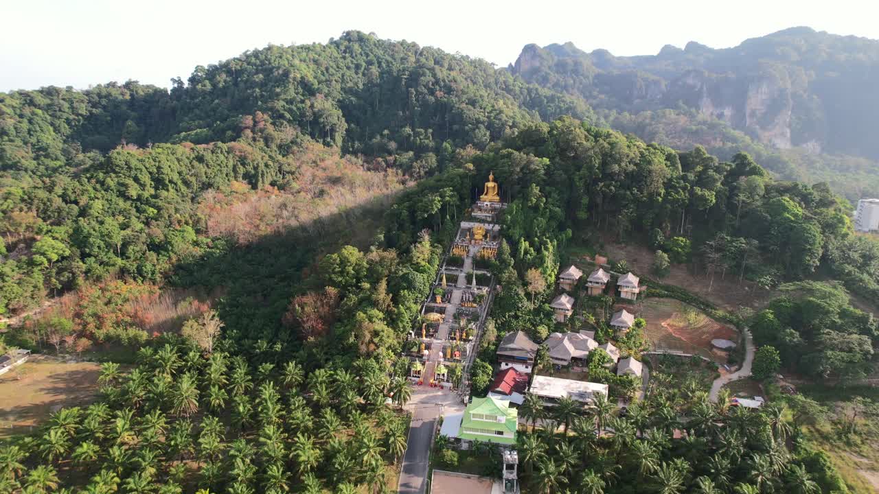 drone aéreo de un templo único con un buda dorado en una montaña rodeada de cocoteros en ao nang krabi tailandia