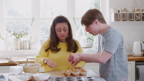 young downs syndrome couple taking homemade cupcakes out of baking tray