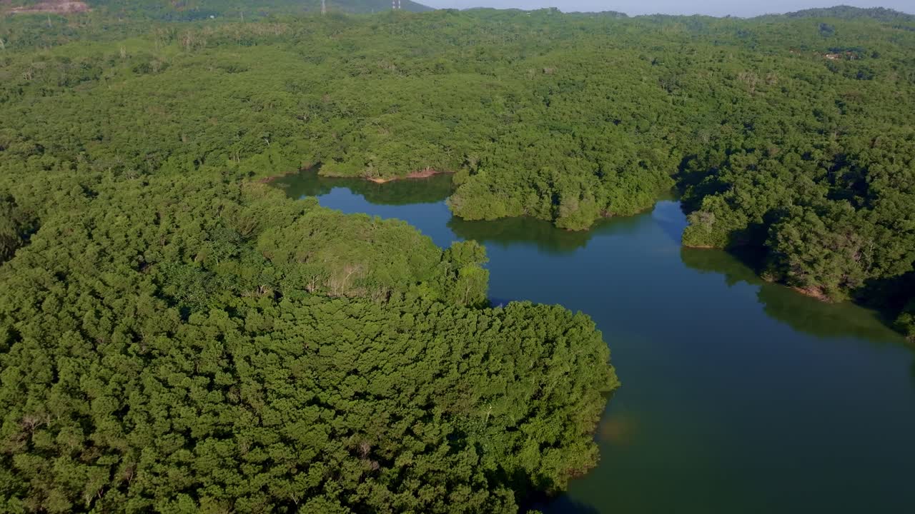Dense green landscape of Rincon Dam with lake in Dominican Republic. Aerial backwards wide shot.