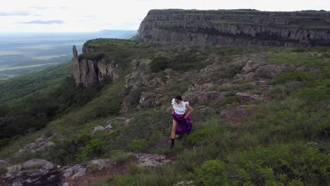 una mujer hispana con un vestido colorido corre por el sendero de la cima del acantilado en el punto de vista