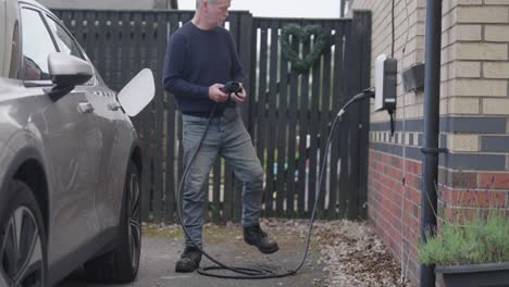 caballero cargando automóvil eléctrico, propiedad familiar al aire libre, cámara lenta