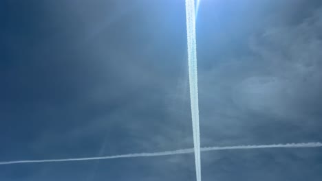 two white jet wakes forming a huge cross in a bright blue sky