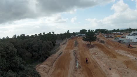 Vista-Trasera-Del-Piloto-De-Motocross-En-La-Pista-De-Tierra-Directamente-Con-El-Cielo-Nublado