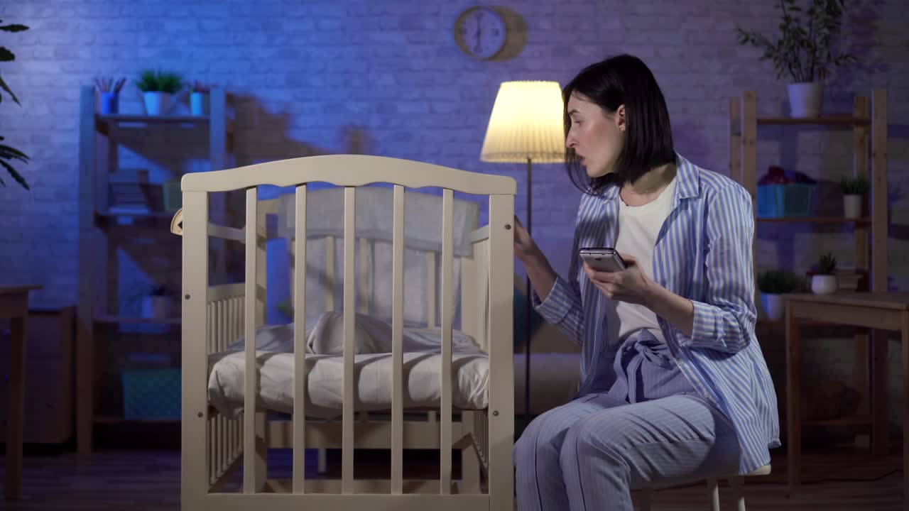 한 젊은 독신 어머니가 손에 든 스마트폰과 신생아를 위해 인터넷을 검색합니다.