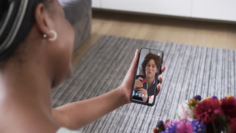 Mujer-Birracial-Sosteniendo-Un-Teléfono-Inteligente-Con-Un-Hombre-Birracial-Con-Flor-En-La-Pantalla