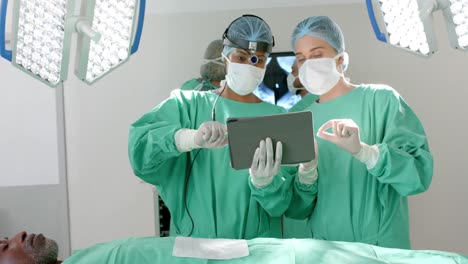 diverse surgeons wearing surgical gowns, using tablet in operating theatre, slow motion