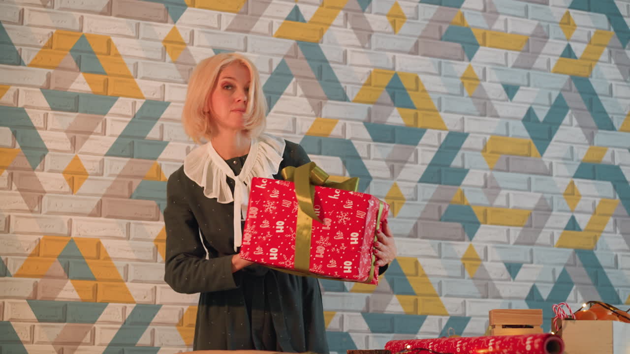 White woman holding red present, patterned brick wall backdrop, wrapping on wooden table with green ribbon, tape and scissors, cozy festive lighting, christmas mood, content creator gift prep, gentle