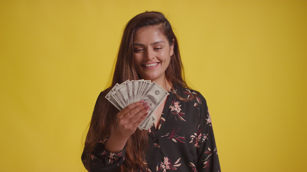 黄色い背景に100ドル紙幣を握って賞金受賞を祝う興奮した女性のスタジオショット