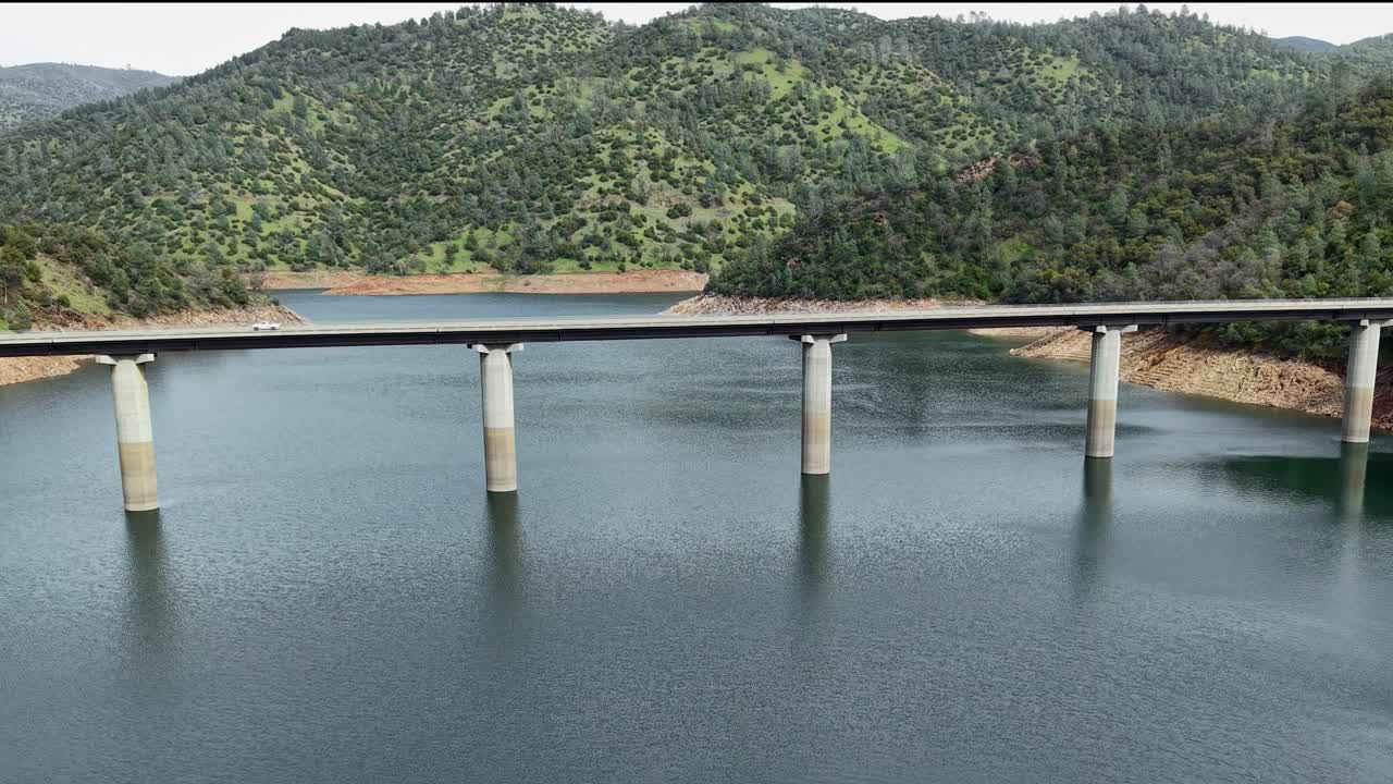 An aerial view of a vehicle making its way over the Don Pedro Reservoir Bridge, with the lake stretching into the distance.