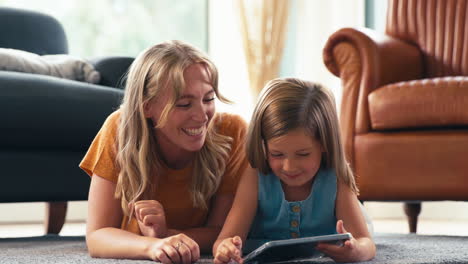 Familie-Mit-Mutter-Und-Tochter,-Die-Zu-Hause-Im-Wohnzimmer-Auf-Dem-Boden-Liegen-Und-Mit-Einem-Digitalen-Tablet-Spielen