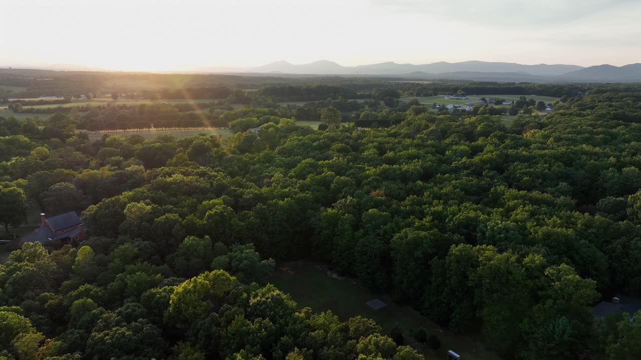Drone flight over idyllic forest landscape and residential area in suburbia or America. Town. Greenery of blue ridge mountains in Virginia. Golden sunset at sky. Wide shot