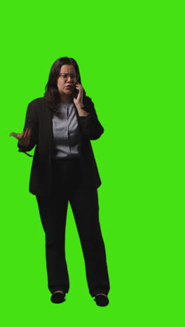 vertical video full length shot of assertive businesswoman talking on mobile phone against green screen background 1