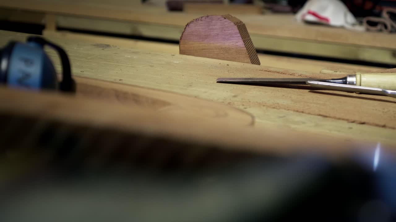 Close view of a carpenter's workbench featuring earmuffs, a chisel, and various wood pieces in a professional workshop. Static slow motion