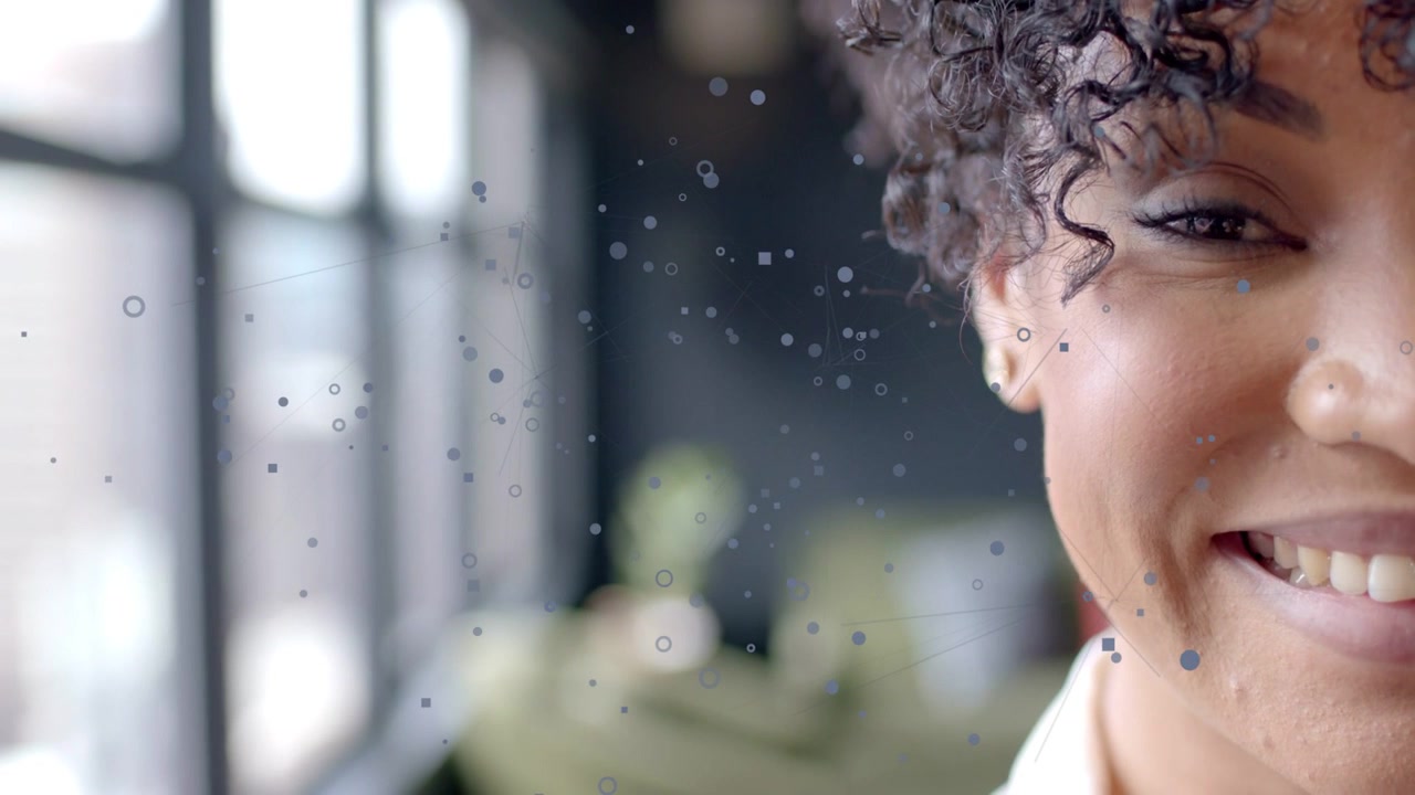 Femme dans un espace de travail technologique réagissant à des particules de données flottantes, ouvrant les yeux et souriant largement