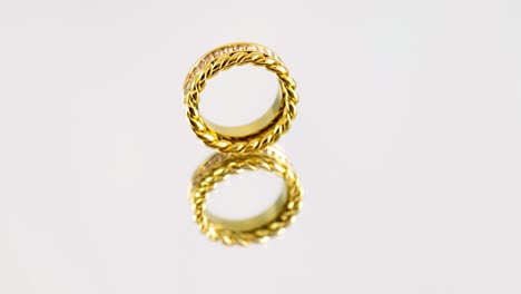 rotating golden knotted sparkly twin golden ring with zircons and its reflection on white background. beautiful valentine's gift.