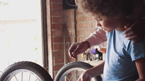 father standing behind his pre teen son helping him use a spanner while making a racing kart together in the garage, side view