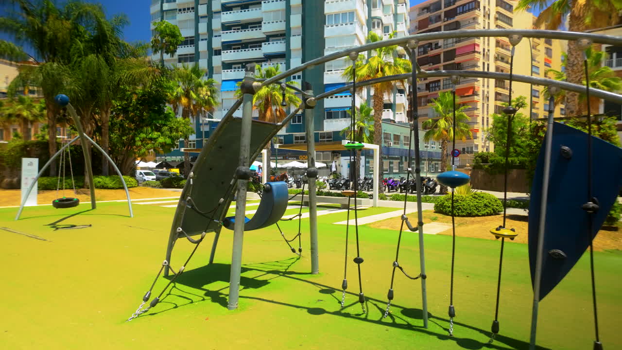 Playground in Malaga's Malagueta park with modern play structures and high-rise buildings in the background - empty space no people