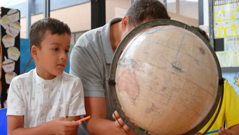 vista frontal de un joven maestro caucásico que enseña a los niños sobre geografía con el globo en el aula 4k
