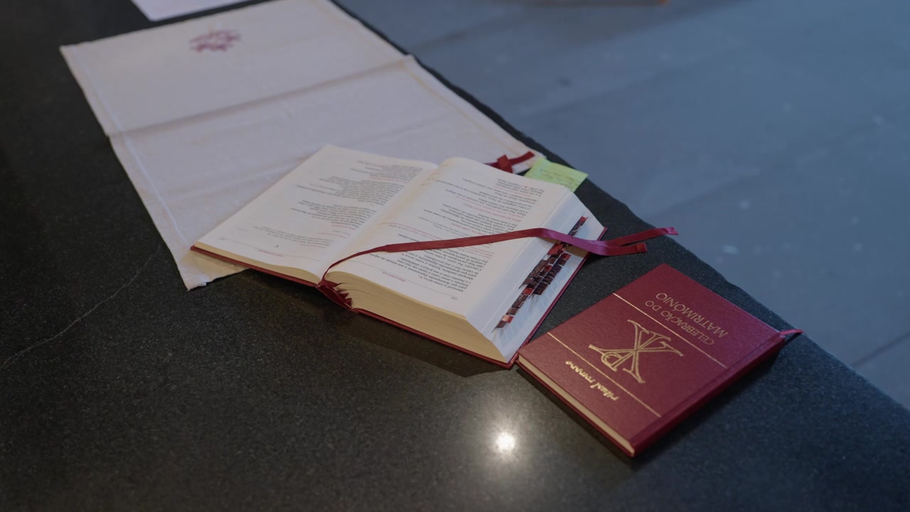 Otevřená liturgická kniha s červenými záložkami vedle červeného misálu na kamenném kostelním oltáři.