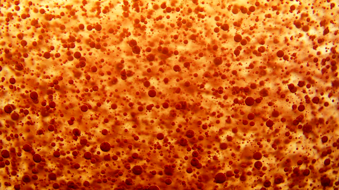 빨간색 잉크 거품이 노란색 밀집 액체에서 천천히 흐르고, 어두운 큰 구에 의해 방해됩니다.