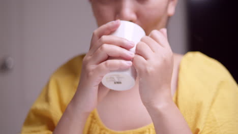 sosteniendo una taza de bebida caliente a su boca, una mujer está bebiendo y bebiendo un poco de la mezcla saludable, mientras rompe en una sonrisa después de tomar un sorbo