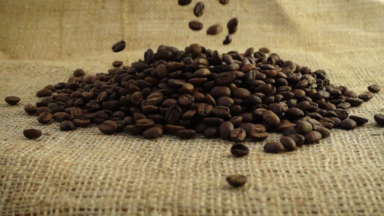 Chicchi di caffè cadono su tela di iuta al rallentatore.