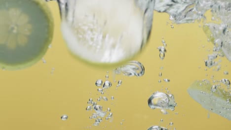 Video-of-slices-of-lime-and-lemon-falling-into-water-with-copy-space-on-yellow-background