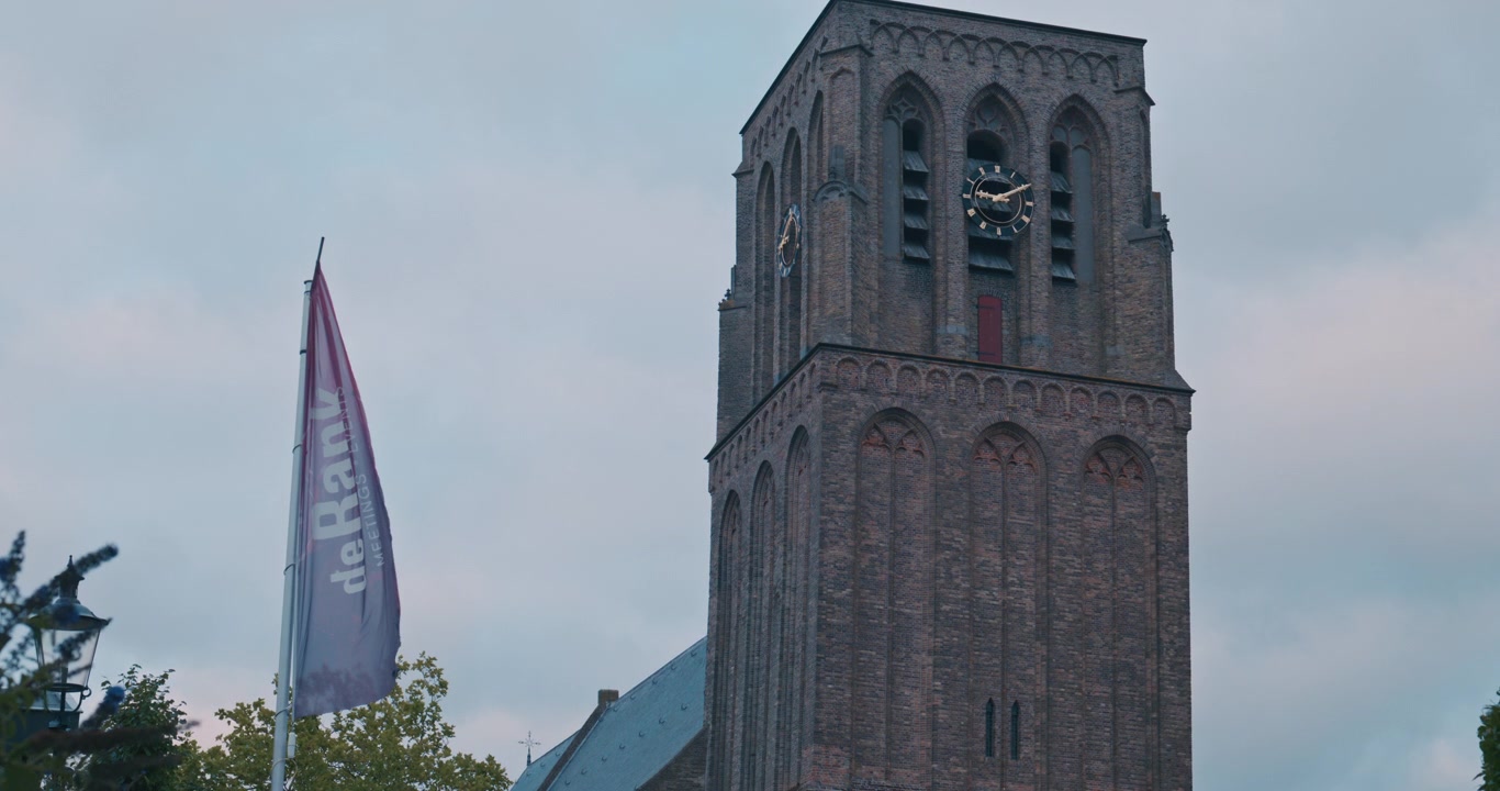 Højt murstenstårn med urskiver og buede vinduer mod overskyet himmel