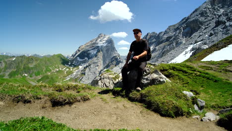 a man under the sun, seated on a rock smoking, with mountain nature in the background