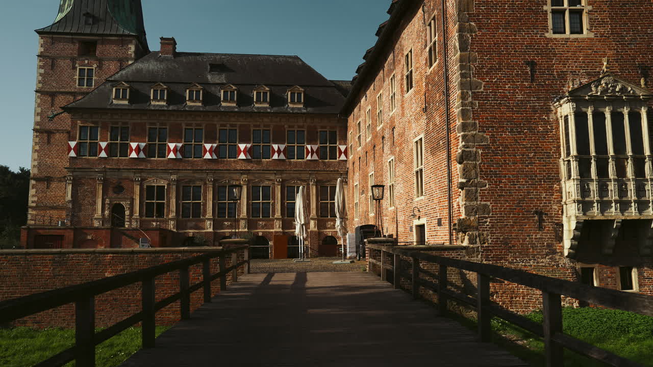 Entrance bridge to Schloss Raesfeld in Germany, framed by two large statues. The medieval castle rises in the background, surrounded by greenery, showcasing historic architecture and charm