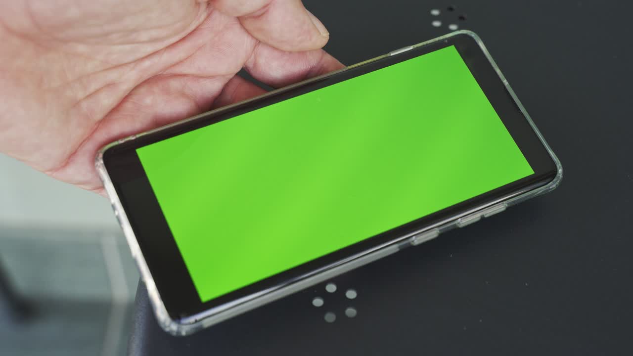 테이블 위 에 녹색 스크린 을 가진 스마트폰 을 들고 있는 사람