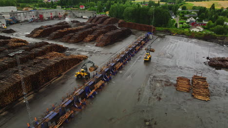 Grapple-loaders-moving-felled-timber-logs-around-in-lumberyard,-aerial-riser