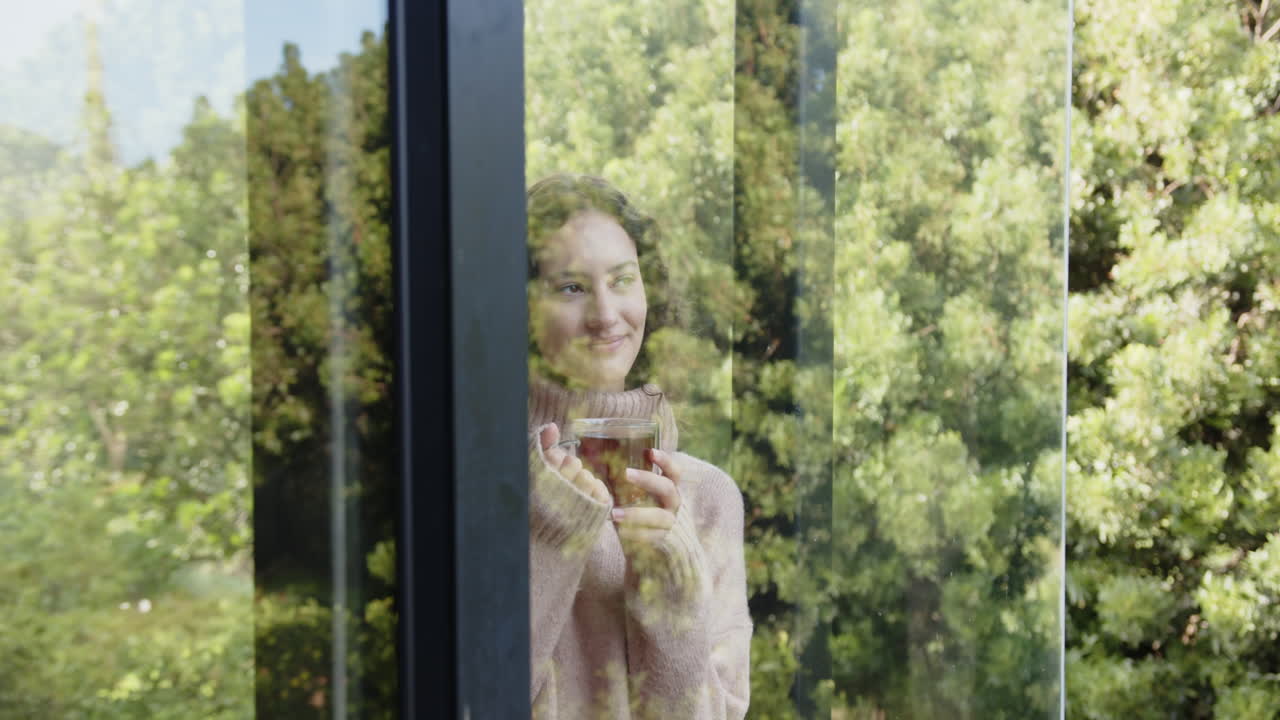 Holding cup of tea, woman relaxing and enjoying view through window, copy space